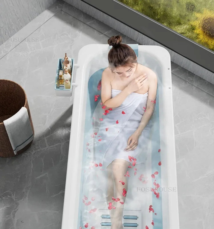 Portable white folding bathtub for adults with water and floating petals, woman relaxing